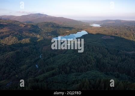 Ban Venue, Loch Achray, Loch Lomond und Trossachs National Park, Schottland. 7. September 2021 IM BILD: Drohnenansicht von Loch Achray aus und in der Ferne, Loch Venachar. Der Schatten von Ben Venue, der sich direkt hinter der Kamera und unter den immergrünen, von Wald bedeckten Ausläufern befindet und bei Tagesausflüglern und Forellen aus aller Welt beliebt ist. Quelle: Colin Fisher Stockfoto