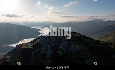 Ban AA’n, Loch Achray, Loch Lomond und Trossachs National Park, Schottland. 7. September 2021 IM BILD: Blick auf die Drohne von oben auf Ben AA’n und die umliegenden Hügel mit dem Loch Katrine Reservoir als Hintergrund mit der untergehenden Sonne, die einige Kletterer auf dem Gipfel des Ben AA’n silhouettiert Quelle: Colin Fisher Stockfoto