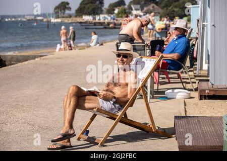 Sonnenanbeter auf ihren Strandhütten in Hamworthy, in der Nähe von Poole, Dorset, genießen die Mini-Hitzewelle im Herbst, England, Großbritannien Stockfoto