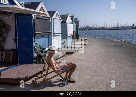 Sonnenanbeter auf ihren Strandhütten in Hamworthy, in der Nähe von Poole, Dorset, genießen die Mini-Hitzewelle im Herbst, England, Großbritannien Stockfoto