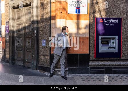 Geschäftsmann lauert hinter der Ecke einer Mauer in der Young Street, Kensington, Central London, Großbritannien Stockfoto