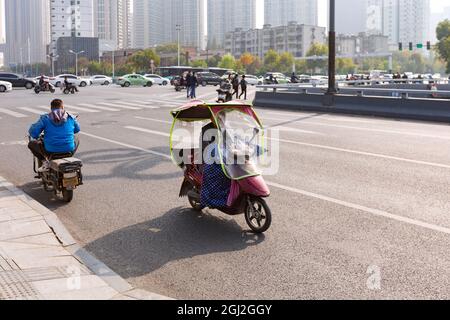 Menschen auf einem elektrischen Fahrrad mit farbenfroher Windschutzscheibe  an der Kreuzung, Hefei, China Stockfotografie - Alamy