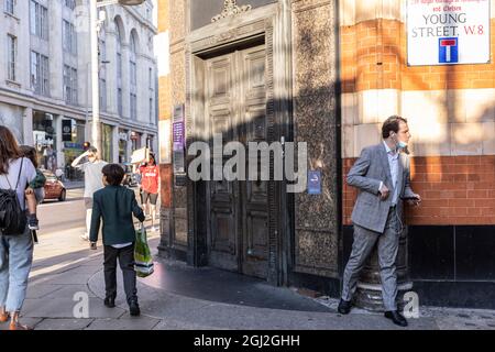 Geschäftsmann lauert hinter der Ecke einer Mauer in der Young Street, Kensington, Central London, Großbritannien Stockfoto