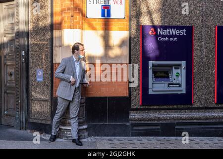 Geschäftsmann lauert hinter der Ecke einer Mauer in der Young Street, Kensington, Central London, Großbritannien Stockfoto