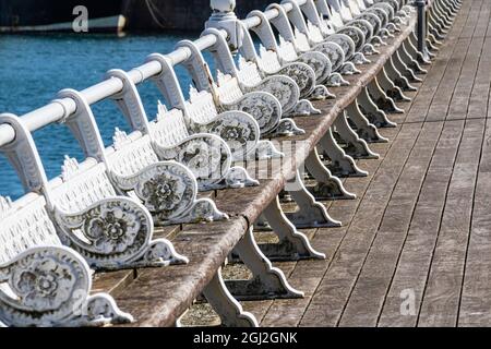 Detail einer Reihe von weißen Bänken und Geländern an der Seite des Torquay Inner Harbour Walkway. Ein beliebter Besucherstopp für Torbay und South Devon. Stockfoto