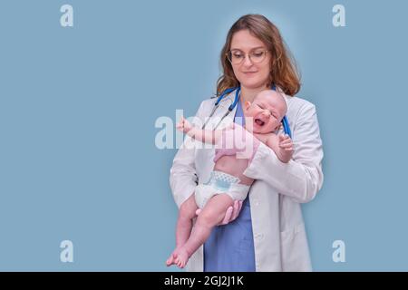 Kinderarzt hält neugeborenes Baby und lächelt, blauer Studiohintergrund. Fröhliche Krankenschwester in Uniform mit einem Baby in den Armen Stockfoto