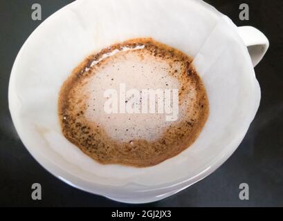 Die Nahaufnahme des arabica-gemahlenen Kaffees während des Brauprozesses aus dem Gießen von heißem Wasser in den Keramiktropfer, schwimmt Crema über dem Kaffee la Stockfoto