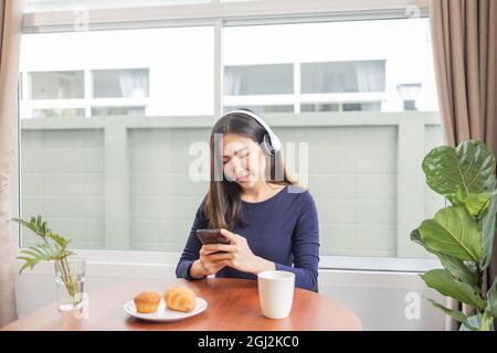 Work from Home Konzept eine junge Frau, die Kopfhörer trägt, genießt einen Moment lang ihre Lieblingsliylist mit Desserts und einem Getränk auf dem Tisch. Stockfoto