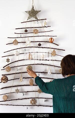 Lange Belichtung, Unschärfe. Rückansicht der Frau Dekoration handgemachte Handwerk Weihnachtsbaum aus Stäben und natürlichen Materialien an der Wand hängen gemacht. Nachhaltige C Stockfoto