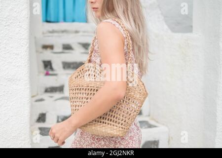 Bild einer gewebten Strohsack-Sommertasche. Trendiges Sommeroutfit. Modell. Kaukasische Frau in legerem Kleid mit gewebtem Strohhalm Sommertasche. Hochwertige Fotos Stockfoto