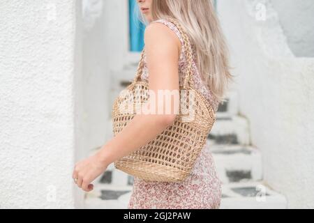Bild einer gewebten Strohsack-Sommertasche. Trendiges Sommeroutfit. Modell. Blonde Frau in legerem Kleid mit gewebter Strohhalmtasche. Hochwertige Fotos Stockfoto