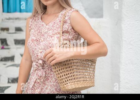 Bild einer gewebten Strohsack-Sommertasche. Trendiges Sommeroutfit. Modell. Kaukasische Frau in legerem Kleid mit gewebtem Strohhalm Sommertasche. Hochwertige Fotos Stockfoto