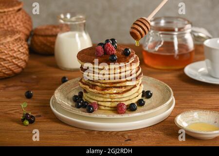 Amerikanische Pfannkuchen mit Honig und Rahm. Schwarze Johannisbeere, Himbeere, Brombeere mit Beeren bestreut. Selektiver Fokus Stockfoto