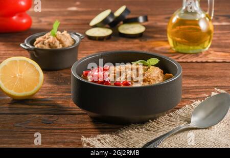 Arabisches Essen Babaganoush Nahaufnahme auf dem Teller und Zutaten auf dem Tisch. Babaganush oder Auberginen-Kaviar. Gebackene Aubergine. Stockfoto