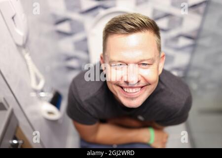 Porträt eines jungen zufriedenen Mannes, der in Nahaufnahme auf der Toilette sitzt Stockfoto