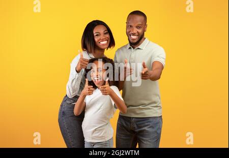 Hey, du. Aufgeregt schwarze Eltern und ihre Tochter zeigen Finger auf die Kamera, wählen und Kommissionierung Sie, isoliert über gelben Studio Backgrou stehen Stockfoto