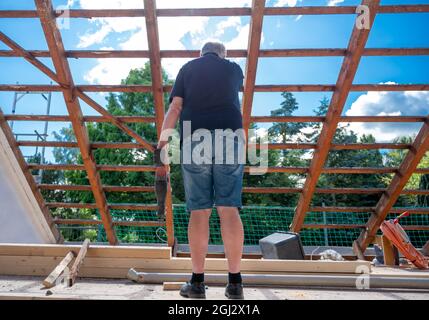 Der alte Mann schneidet den Rahmen eines neuen Fensters auf dem Dach eines Privathauses aus. Ein Do-it-yourself-Projekt. Stockfoto