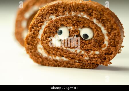 Schokoladen-Biskuitrolle mit Vanillegeschmack, Füllung mit dekorieren süßen Augen, Schokolade schweizer Rolle, lustiges Essen Stockfoto