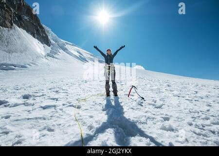 Die Frau hob ihre Arme und lächelte fröhlich, während sie den Mont Blanc (Monte Bianco) in Bergsteigerkleidung mit einem Kletterha besteigte Stockfoto