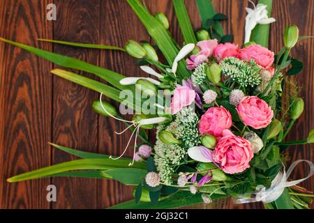 Bouquet von rosa weiß grünen Blumen auf Holzhintergrund angeordnet. Rosen, Sedum, Hosta, Samenkapseln, Gomphrena und Gräser Stockfoto