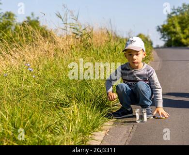 POZNAN, POLEN - 05. Sep 2021: Kleiner Junge, der neben einem Grasfeld auf einer asphaltierten Straße kniet. Stockfoto