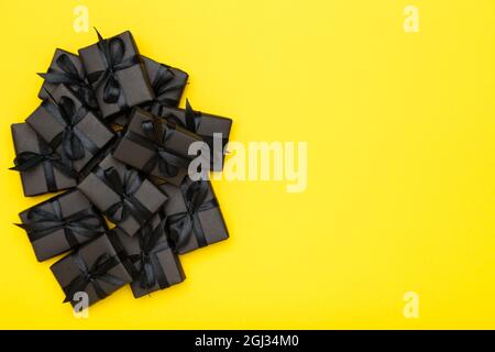 Schwarze Geschenkschachteln mit schwarzen Bändern auf hellem, sattem gelbem Hintergrund. Black Friday Sale flat lay, Draufsicht, Kopierfläche Stockfoto
