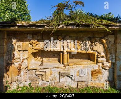 Fragmente der geschnitzten Steinarbeiten der Hailes Abbey, eingebettet in die Wand des Friedhofs der St. Peter’s Church neben dem Stanway House, Cotswolds, England Stockfoto