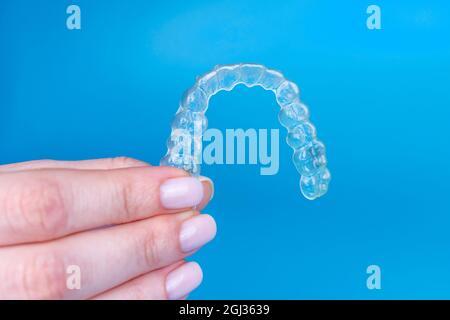 Hand hält abnehmbare unsichtbare transparente Aligner invisalign oder Kunststoff kieferorthopädischen Zahnspangen Halter auf blauem Hintergrund Stockfoto