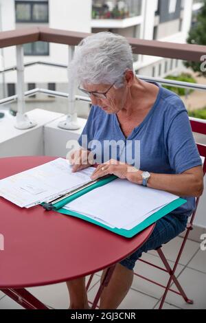 Eine ältere Frau liest schriftliche Verwaltungsdokumente, die an einem Tisch sitzen Stockfoto