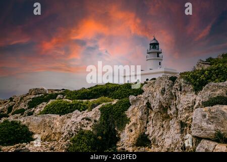 Blick auf den Leuchtturm von Cavalleria mit felsigen Klippen während des dramatischen bewölkten Sonnenuntergangs auf der baleareninsel Menorca in Spanien Stockfoto