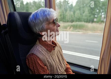Seriöse ältere kaukasische Frau mit Sonnenbrille, die durch das Fenster schaut, während sie im Bus fährt Stockfoto