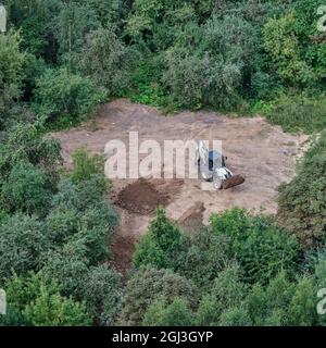 Der Bagger bereitet den Boden auf dem Feld im Wald unter den Bäumen für die Landschaftsgestaltung und Landwirtschaft, Draufsicht - Moskau, Russland, 24. August 2021 Stockfoto