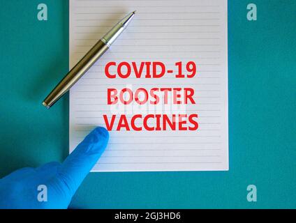 Covid-19 Booster Schüsse Impfstoffe Symbol. Weiße Note mit Worten Covid-19 Booster Vaccines, schöner blauer Hintergrund, Arzthand und Metallstift. Covi Stockfoto