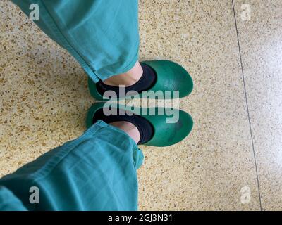 Ein Bild der gestreckten Beine in grüner OP-Kleidung und OP-Schuhen Stockfoto