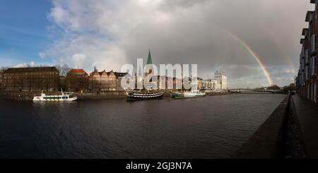 Blick auf das historische Viertel mit Lagerhäusern und alten Segelbooten in Bremen, Deutschland und einem schönen Regenbogen und stürmischen Wolken Stockfoto