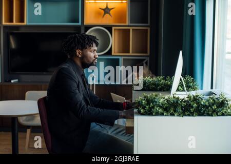 Dunkelhäutiger Geschäftsmann in einem dunklen Anzug arbeitet bei einem Computer in einem modernen Büro Stockfoto