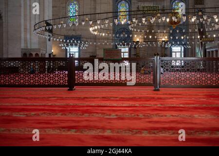 Aufnahme eines Moscheeinnenraums mit runden Lampen, rotem Teppich zum Beten und einem Holzzaun Stockfoto