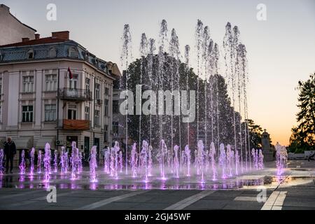 NIS, Serbien - 07. September 2021 Altes Gebäude und Brunnen auf dem Stadtplatz mit violettem Wasser bei Sonnenuntergang an einem Herbsttag in der Stadt Nis Stockfoto