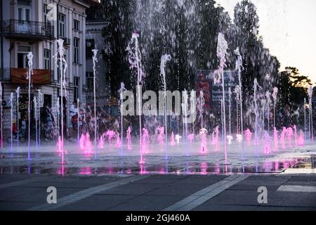 NIS, Serbien - 07. September 2021 Ein leuchtender Brunnen auf dem Stadtplatz mit purpurem Wasser bei Sonnenuntergang an einem Herbsttag in der Stadt Nis Stockfoto
