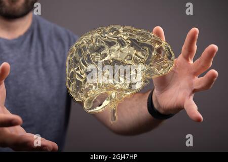 3D-Darstellung eines goldenen menschlichen Gehirns, das in der Luft schwebt, wobei ein Mann seine Hände um das Gehirn hält Stockfoto