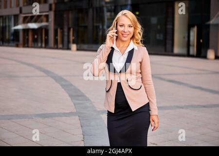 Attraktive Geschäftsfrau, die in der Nähe eines Bürogebäudes telefoniert. Stockfoto