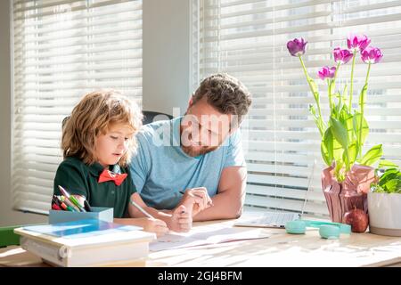 Glücklicher bärtiger Vater, der Schulaufgaben mit seinem Sohn im Klassenzimmer schrieb und Heimschooling machte Stockfoto