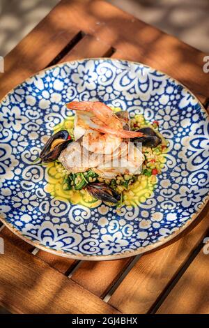 Draufsicht auf einen dekorierten blauen Majolika-Teller mit Hühnchen-kleinen Stücken auf einer sonnigen Holzfläche Stockfoto