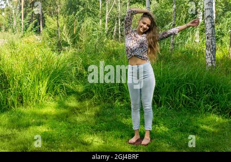 Die junge Frau steht barfuß auf einem Brett mit Nägeln und praktiziert im Freien Yoga Stockfoto