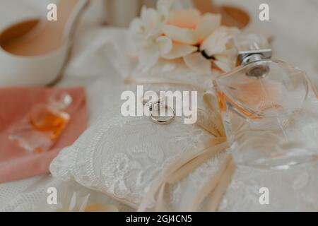 Kissen mit einem Paar Eheringe und Parfüm, umgeben von anderen Hochzeitsparadien auf dem Tisch Stockfoto