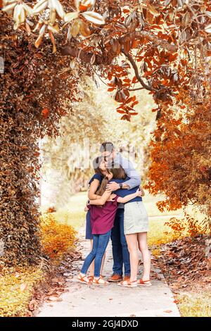 Eine Familie mit Mutter, Vater und zwei Töchtern, die im Herbst draußen auf dem Bürgersteig stehen Stockfoto