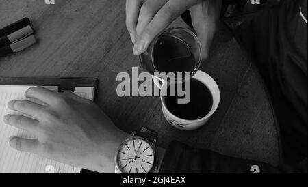 WONOSOBO, INDONESIEN - 07. Apr 2021: Eine Draufsicht von einer Person, die eine Tasse schwarzen Kaffee auf einem Holztisch in Graustufen genießt Stockfoto