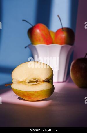 Vertikale Aufnahme eines Apfels in einem Behälter auf einem rosa und blauen Hintergrund Stockfoto