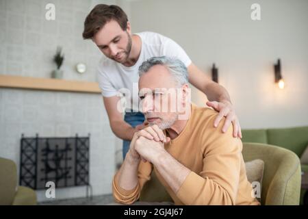 Reifer Mann sieht traurig aus, sein Sohn unterstützt ihn Stockfoto