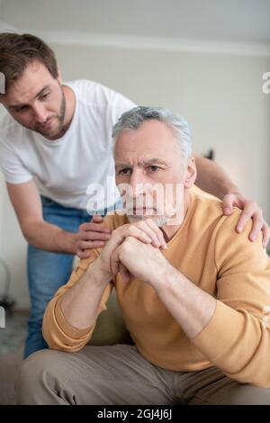 Reifer Mann sieht traurig aus, sein Sohn unterstützt ihn Stockfoto